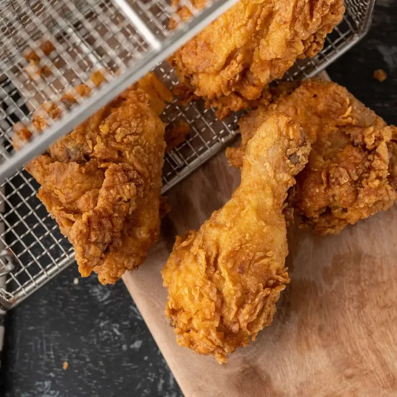 Fried chicken tipped from a wire fry basket onto a wooden board