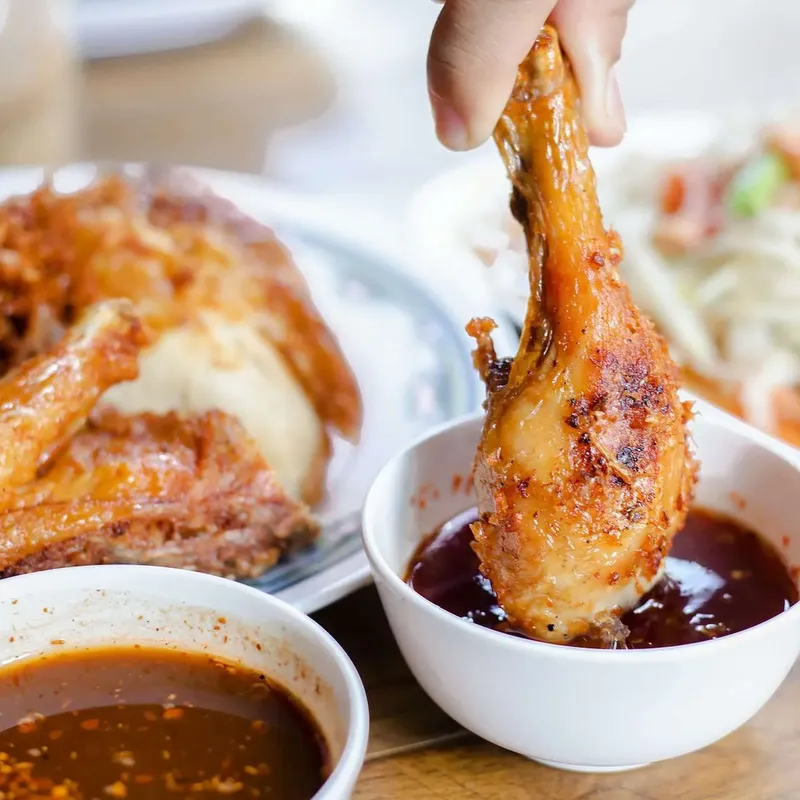 A chicken drumstick dipped into a bowl of dark sauce